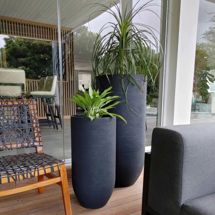 Two large black planters with plants on a patio area.