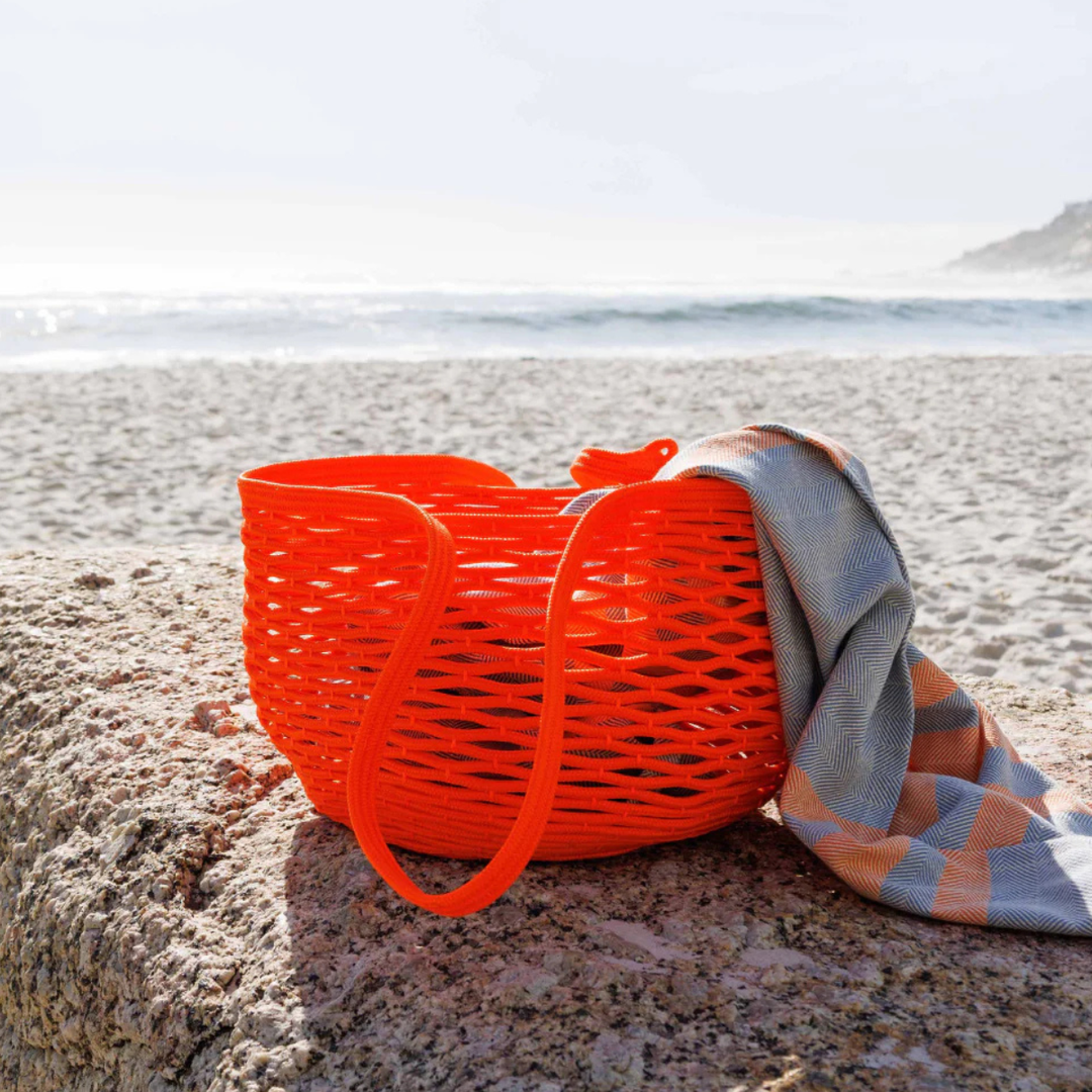 Orange woven bag with a striped towel on a rock by the beach