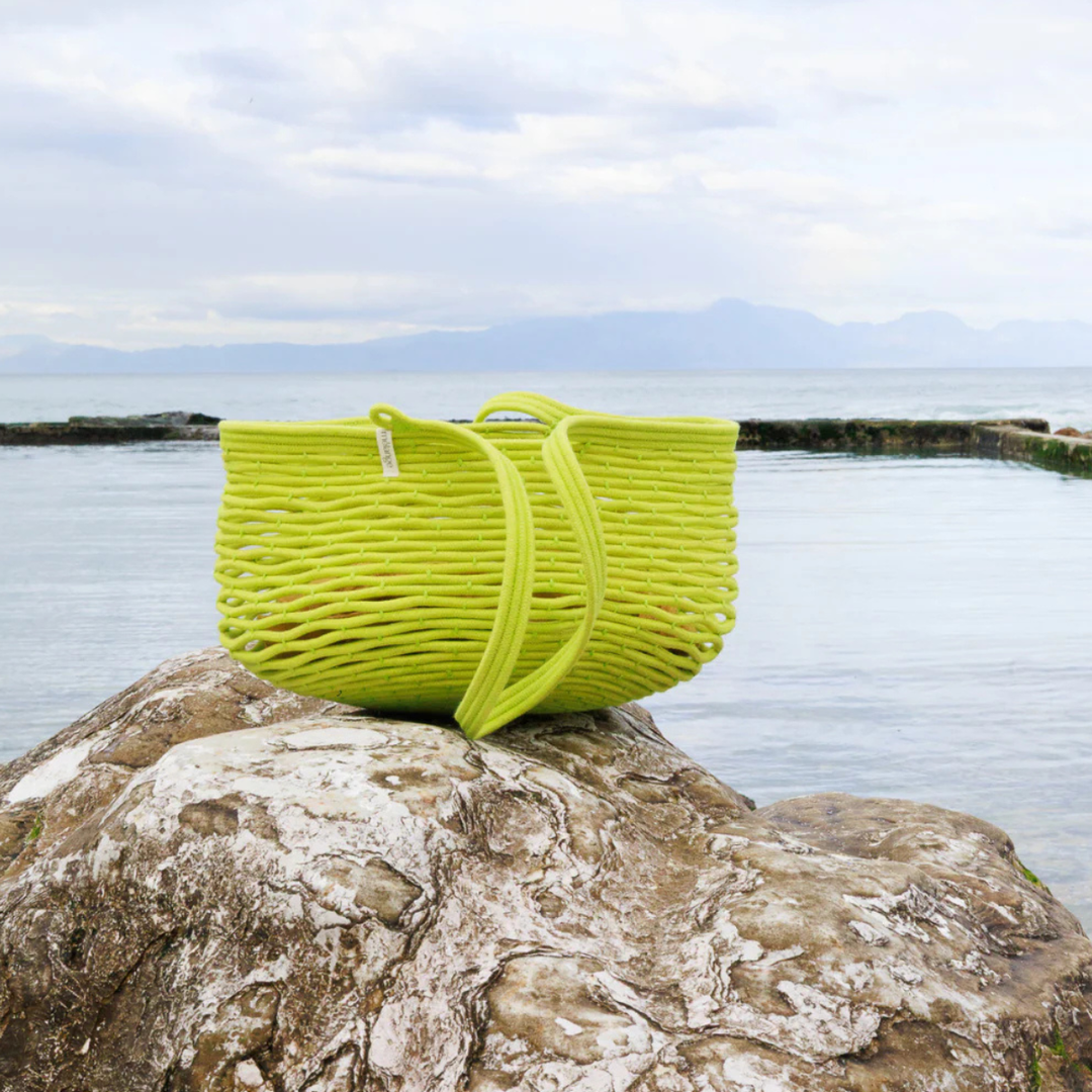 Pistachio woven baskets on a rock by a body of water with mountains in the background.
