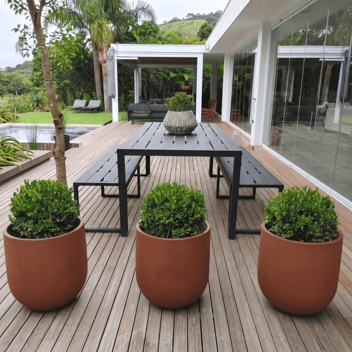 Rustic Cask Planter - Corten Steel displayed on a modern patio with lush greenery and a sleek table.
